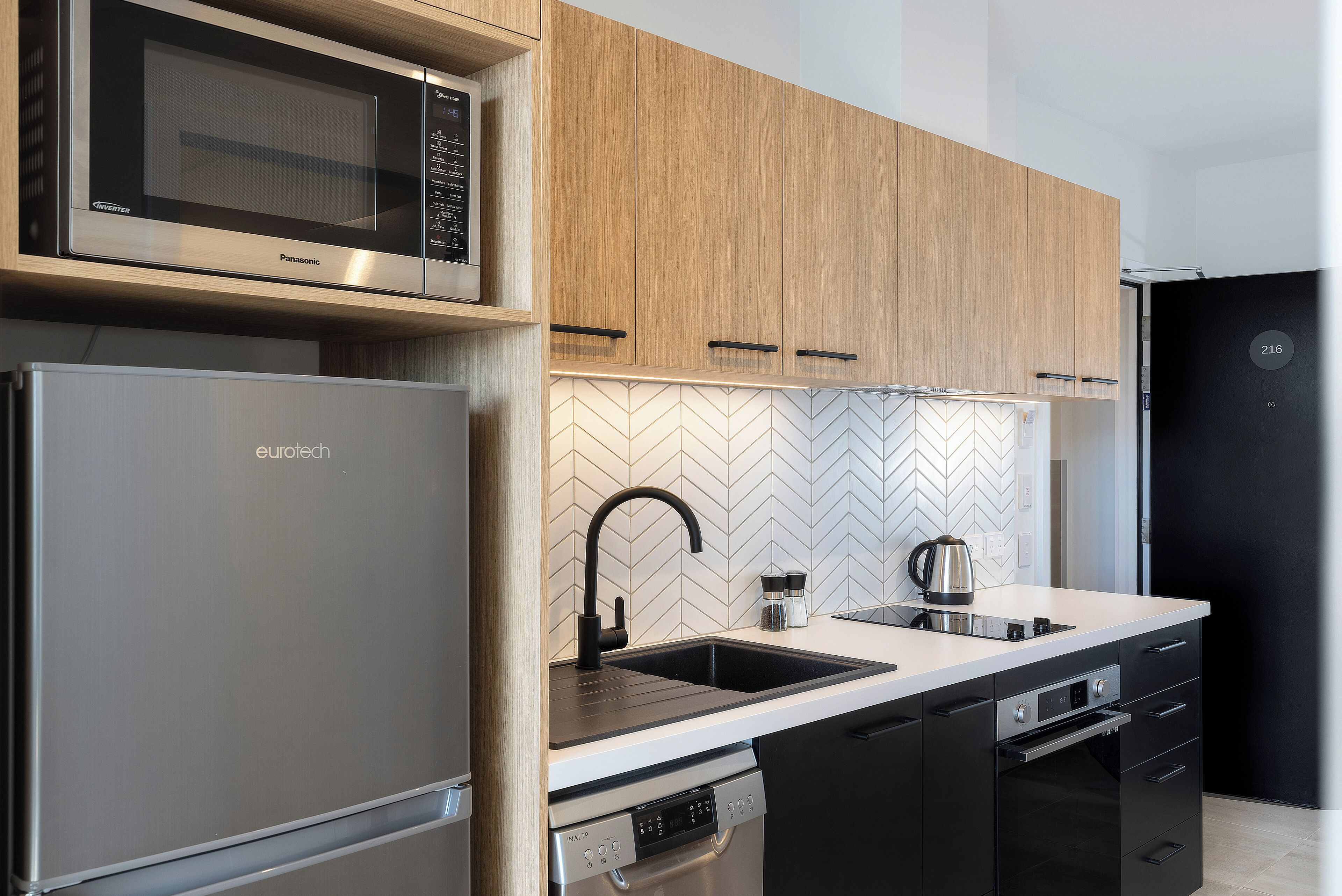 A modern kitchen with a built-in microwave, stainless steel refrigerator, and black dishwasher.