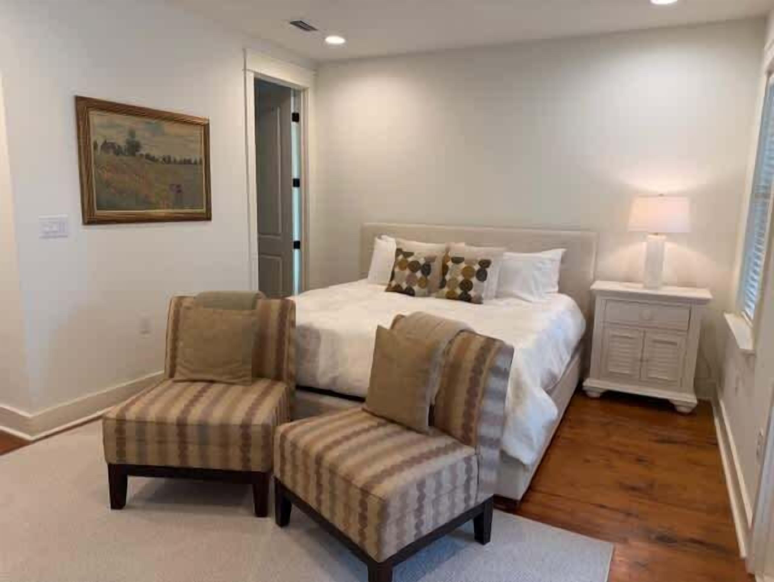 A bedroom with a bed, two armchairs, a nightstand, a lamp, and a painting on the wall.