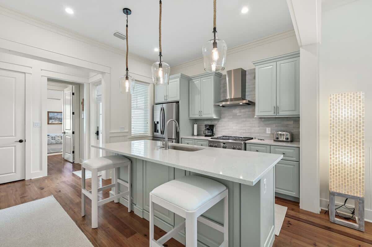 A modern kitchen with white cabinetry, a central island with stools, stainless steel appliances, and pendant lighting.