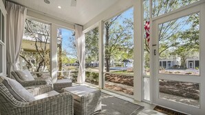 A sunlit room with wicker furniture, large windows, and a view of a residential area. - Watercolor House: Beach Access, & Family Fun! (Santa Rosa Beach)