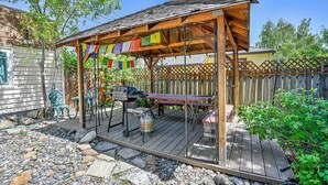 A wooden outdoor patio with a grill, picnic table, and colorful prayer flags. - Charming 4BR Home in a Great Downtown Location (Mount Shasta)