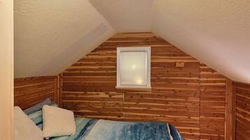 Een slaapkamer met een houten plafond, een raam en een bed met een blauwe deken.