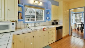 A kitchen with white cabinets, a microwave, a sink, and a window. - Charming 4BR Home in a Great Downtown Location (Mount Shasta)