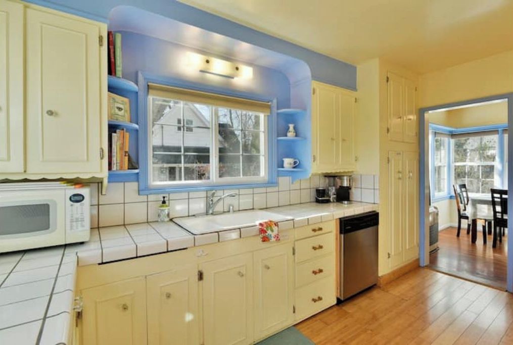 A kitchen with white cabinets, a microwave, a sink, and a window.