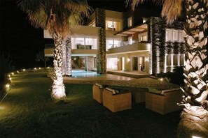 A multi-story building with a swimming pool, outdoor seating, and a well-lit entrance.
