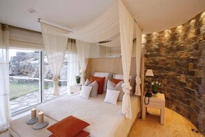 A bedroom with a large bed, a stone wall, and a view of the outdoors.