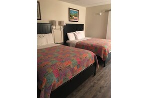 Two single beds with patterned bedspreads are positioned against a wall with a dark headboard, accompanied by a framed picture.