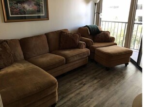Relax in this inviting living space with a comfortable sofa and ottoman, surrounded by a large window offering a view of the outdoors.