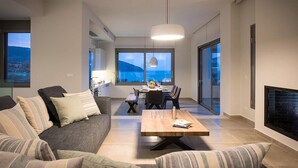 Ein modernes Wohnzimmer mit einer Couch, einem Couchtisch und einem Kamin. Im Hintergrund befindet sich ein Essbereich mit Tisch und Stühlen.