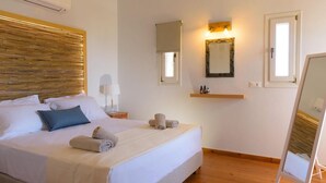 Une chambre d’hôtel avec un grand lit, une table de chevet avec une lampe, un miroir et une étagère avec des articles de toilette.