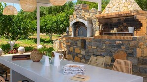 Une cuisine extérieure avec des murs en pierre et une cheminée, entourée de verdure.