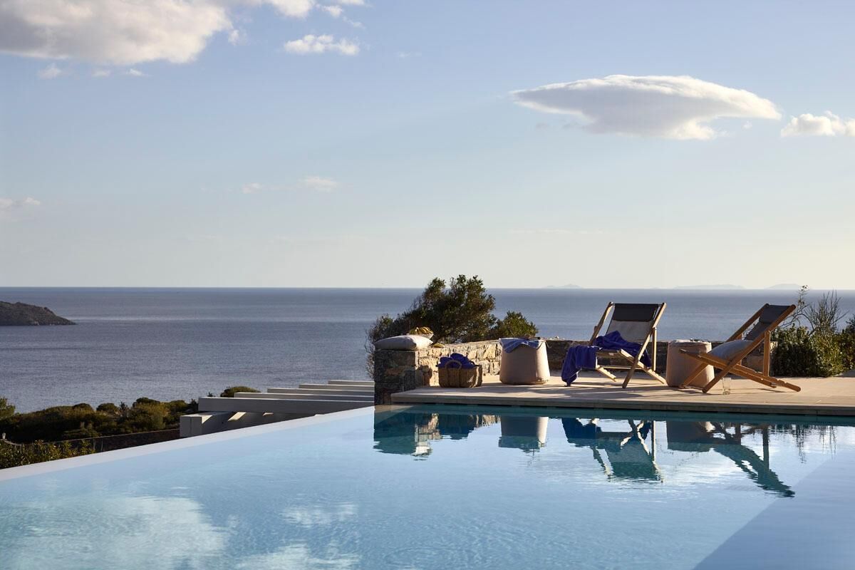 Ein Pool ohne Ende mit Liegestühlen und einer Steinmauer mit Blick aufs Meer.