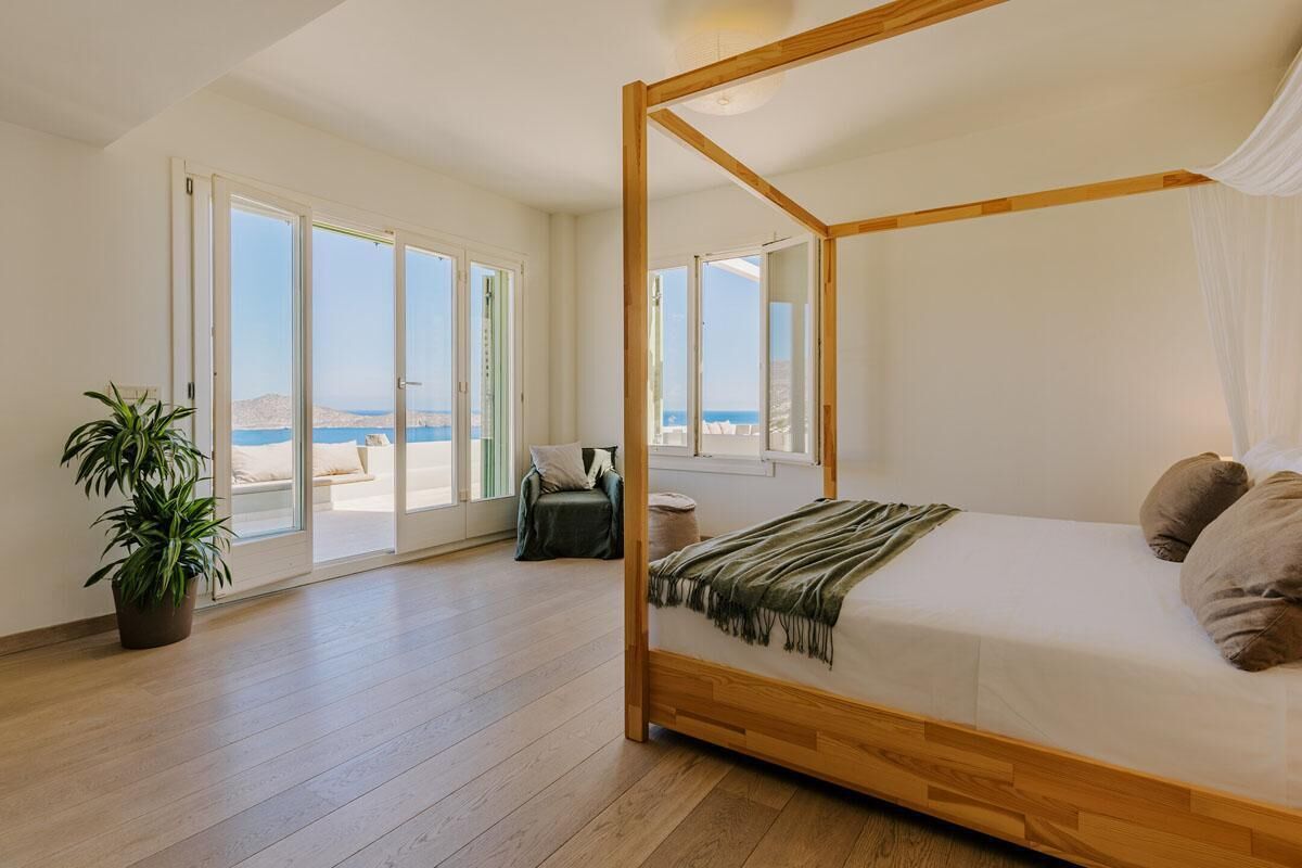 Une chambre spacieuse avec un lit à baldaquin, de grandes fenêtres et une vue sur la mer.