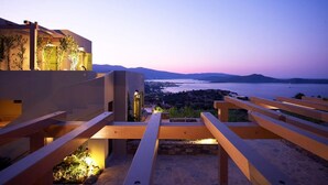 A modern building with a staircase leading to a balcony overlooking a body of water and distant mountains. - Villa Queen with a heated pool (Elounda)
