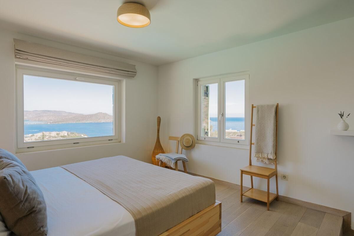 Une chambre avec un lit, deux fenêtres donnant sur la mer, une guitare et une chaise.