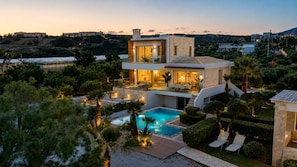 A modern villa with a swimming pool, outdoor seating, and a view of the surrounding landscape.