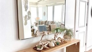 A hallway with a wooden console table holding decorative items and a mirror reflecting a room with a ceiling fan and a plant. - La Playa 1101 Luxury Perdido Key Condo, Breathtaking Views (Pensacola)