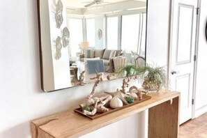 A hallway with a wooden console table holding decorative items and a mirror reflecting a room with a ceiling fan and a plant. - La Playa 1101 Luxury Perdido Key Condo, Breathtaking Views (Pensacola)