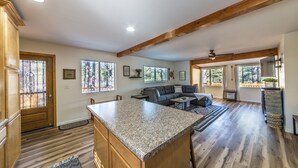 Amplia sala de estar con alto techo de viga de madera, isla de cocina y zona de descanso con sofá y mesa de centro.