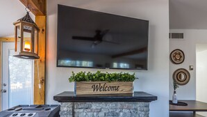 Una sala de estar moderna con una chimenea de piedra, un televisor de pantalla plana montado en la pared y un cartel con la palabra 'Welcome' sobre la repisa.