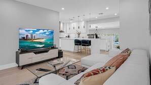 A modern living room with a flat-screen TV, a sofa, a coffee table, and a kitchen area with bar stools. - Casa la Miami, Centrally Located w/ Pool & Gym (Miami)