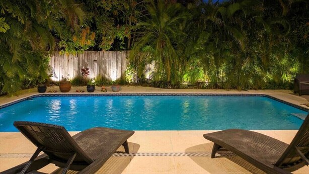 A swimming pool with two lounge chairs, surrounded by lush greenery and a wooden fence. - Casa la Miami, Centrally Located w/ Pool & Gym (Miami)