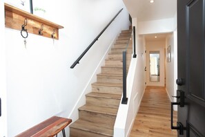 A wooden staircase with a black handrail and a wall-mounted shelf with hooks.