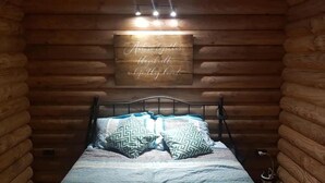 Dormitorio tipo cabaña de madera con estructura de cama metálica, almohadas estampadas y una pared de madera con una cita motivacional.
