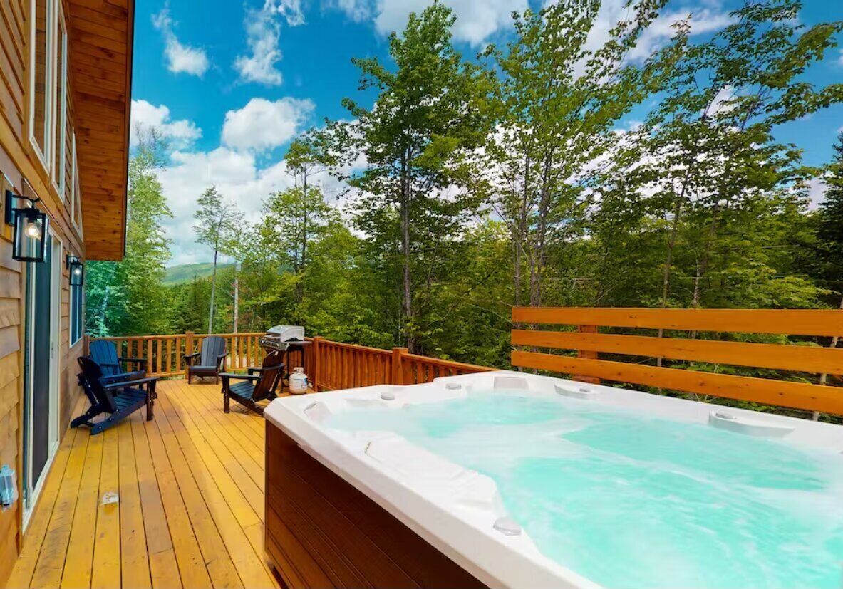 Un terrazzo in legno con idromassaggio, area relax all'aperto e vista su alberi e colline.