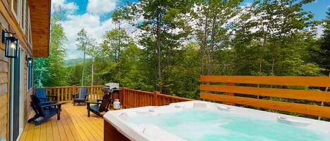 Un terrazzo in legno con idromassaggio, area relax all'aperto e vista su alberi e colline.