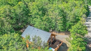 Vista aérea de uma cabana cercada por floresta densa, com um deck visível e área de estar externa.