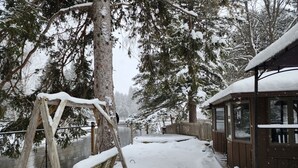 En gungställning i trä och en stuga med ett snötäckt tak, omgiven av snötyngda träd och ett trästaket.