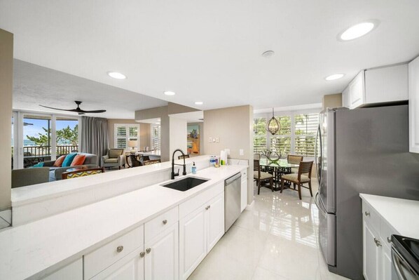 A modern kitchen with white cabinetry, a stainless steel refrigerator, and a dining area with a glass table and chairs.