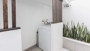Een kleine wasruimte met een wasmachine, een houten leuning en een potplant.