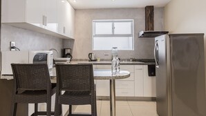 Een moderne keuken met een ronde tafel, twee rieten stoelen, een koelkast en een raam boven de gootsteen.