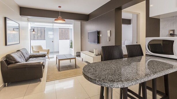 Een moderne woonkamer met een donker leren bank, een ronde granieten tafel en een aan de muur bevestigde televisie.