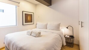 Een moderne slaapkamer met een groot bed, een nachtkastje, een lamp en een ingelijst schilderij aan de muur.