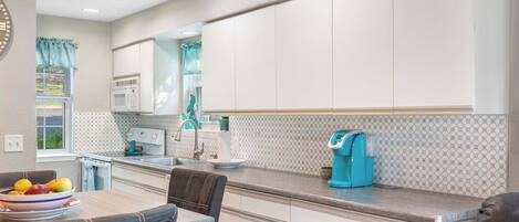 A modern kitchen with white cabinets, a grey countertop, and a blue coffee maker.