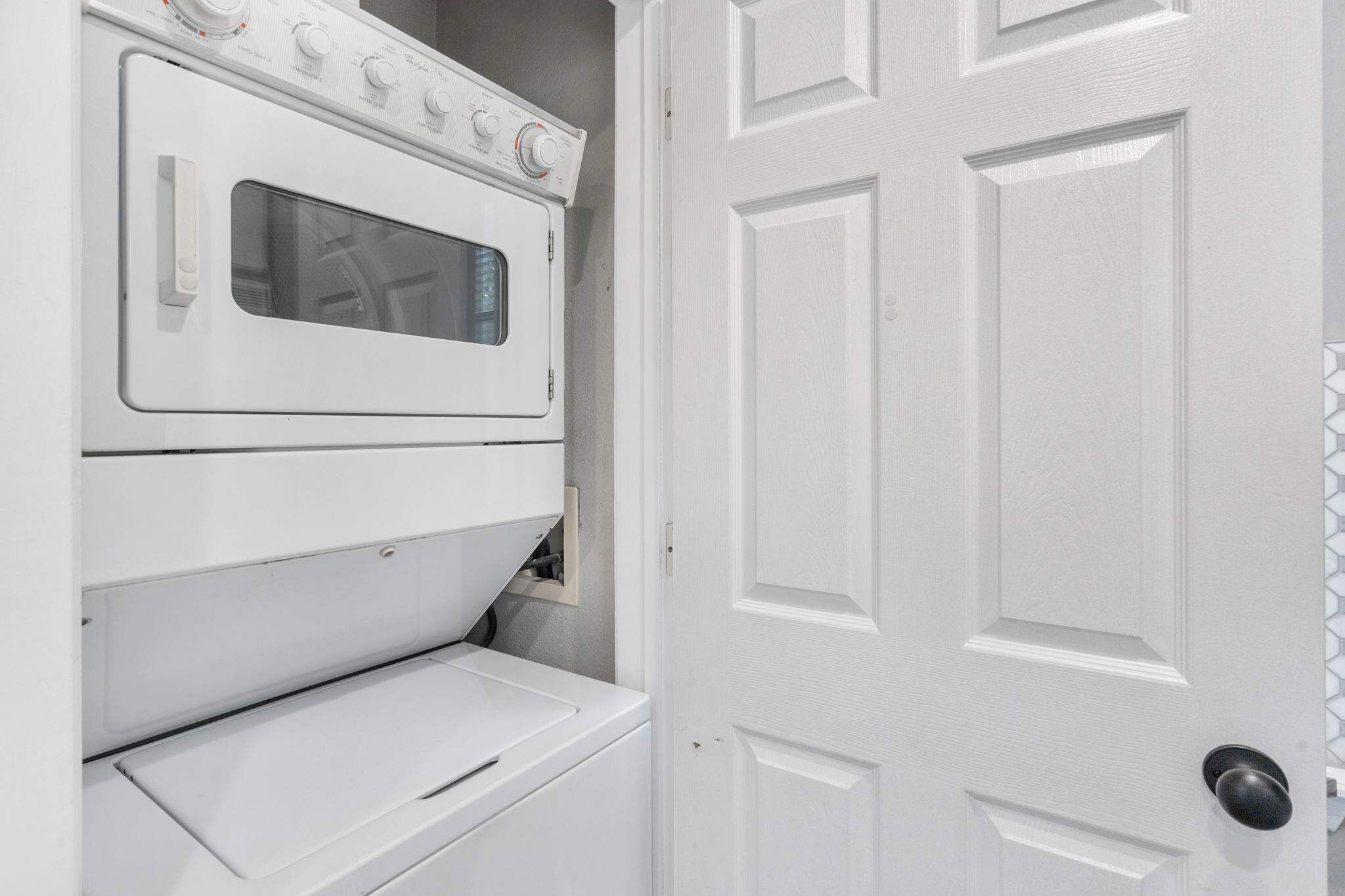 A white laundry room with a built-in washer and dryer, a door with a black handle, and a tiled backsplash.