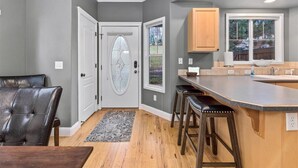 A kitchen with a grey wall, wooden cabinets, a large window, and a bar area with stools.