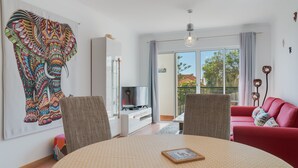 A modern living room with a large elephant tapestry, a red sofa, and a dining area with a round table. - Alta Garajau II (Santa Cruz)