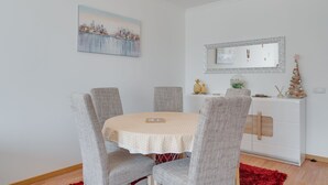 A dining area with a round table, grey upholstered chairs, a white cabinet with decorative items, and a cityscape painting on the wall. - Alta Garajau II (Santa Cruz)
