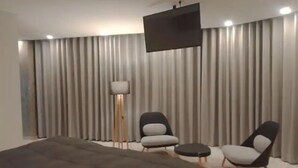 A modern living room with a large bed, two armchairs, a small table, a floor lamp, and a TV mounted on the wall. - Beautiful Penthouse in the best area of the LP city (Zona Calacoto La Paz)