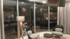 A modern living room with a city view, featuring two armchairs, a floor lamp, and a flat-screen TV. - Beautiful Penthouse in the best area of the LP city (Zona Calacoto La Paz)