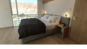 A modern bedroom with a large bed, a nightstand, and a view of a mountainous landscape through a large window. - Beautiful Penthouse in the Best Area of the City (Zona Calacoto La Paz)