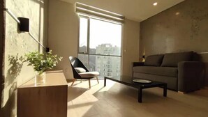 A modern living room with a sofa, a chair, a coffee table, and a large window offering a city view. - Beautiful Penthouse in the Best Area of the City (Zona Calacoto La Paz)