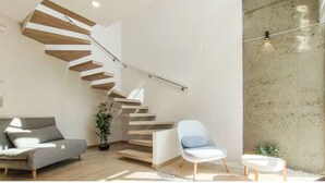 Un intérieur moderne avec un escalier en colimaçon, un canapé gris, une chaise blanche et un mur en béton.