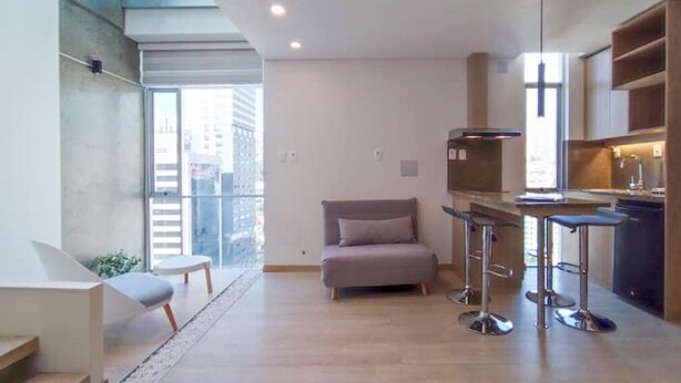 Un appartement moderne doté d’un balcon, d’une kitchenette, d’un canapé gris et d’un coin bar.