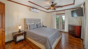 A bedroom with a bed, a nightstand, a ceiling fan, a TV, and a wooden dresser. - Exclusive Full House near Beaches & Downtown (Roatan)