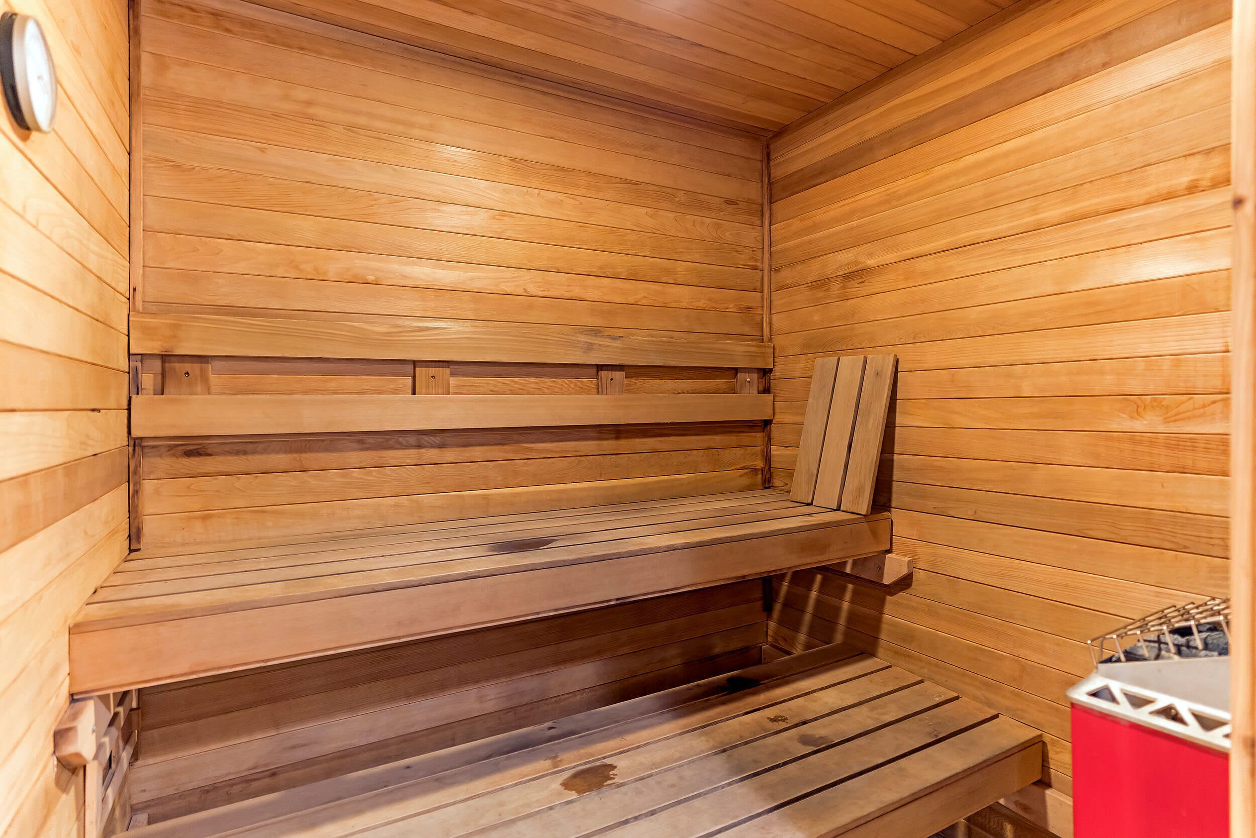 Una sauna con bancos de madera y un recipiente rojo, probablemente para toallas o artículos de aseo.